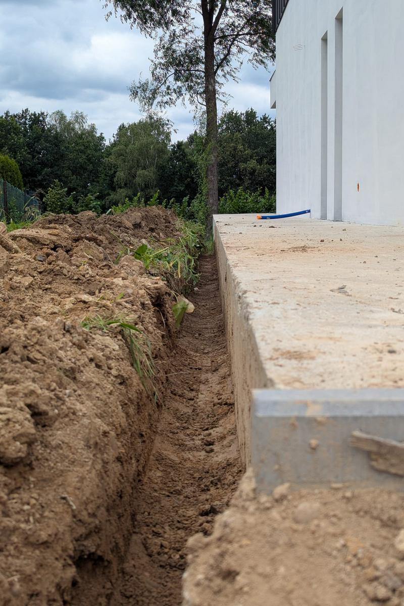 Wykopy i układanie podziemnych rur do nawadniania ogrodu wzdłuż elewacji domu.