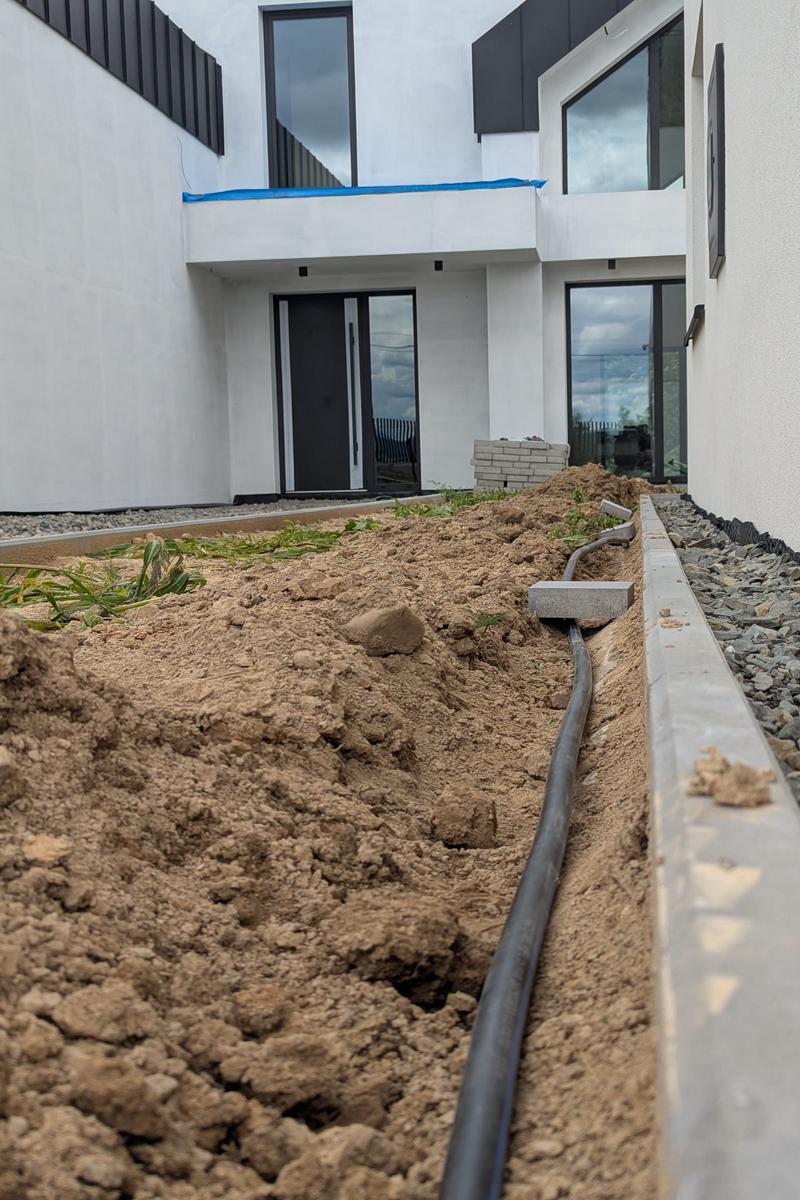 Prace ziemne i montaż rur instalacji automatycznego nawadniania na dużej działce.