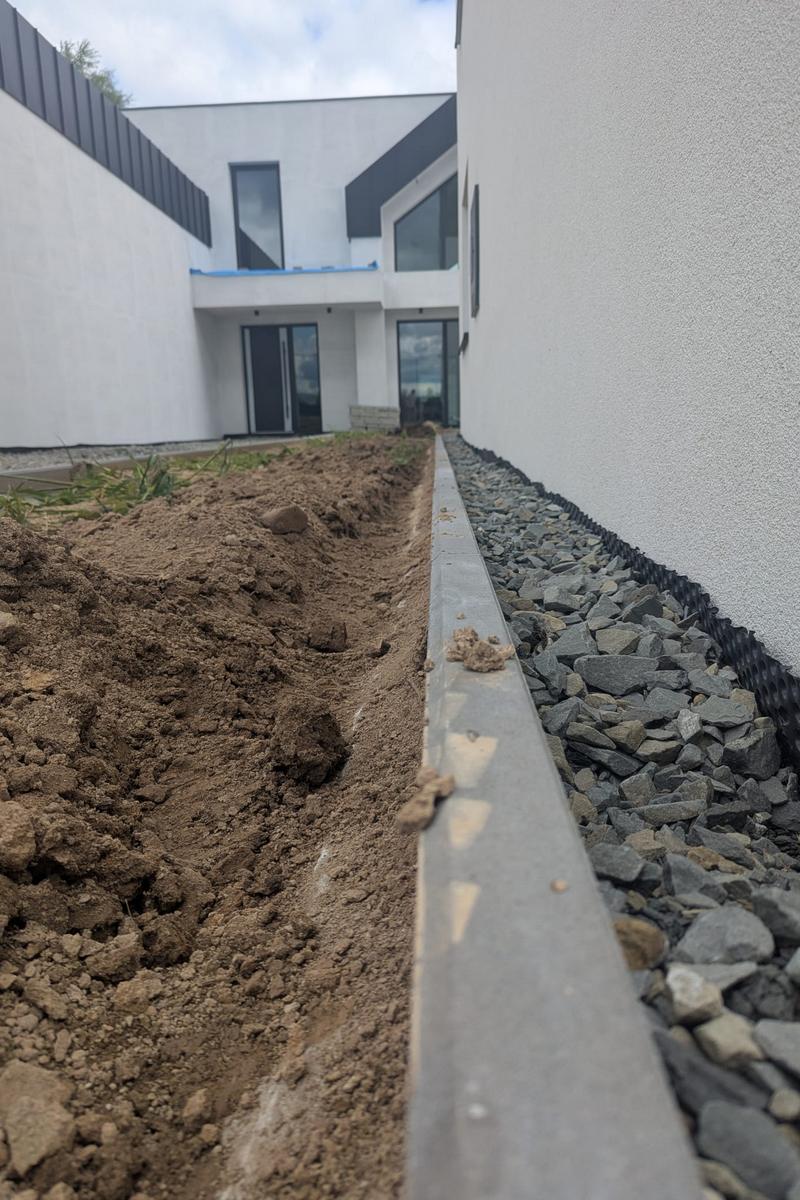 Wykopy i układanie podziemnych rur do nawadniania ogrodu wzdłuż elewacji domu.